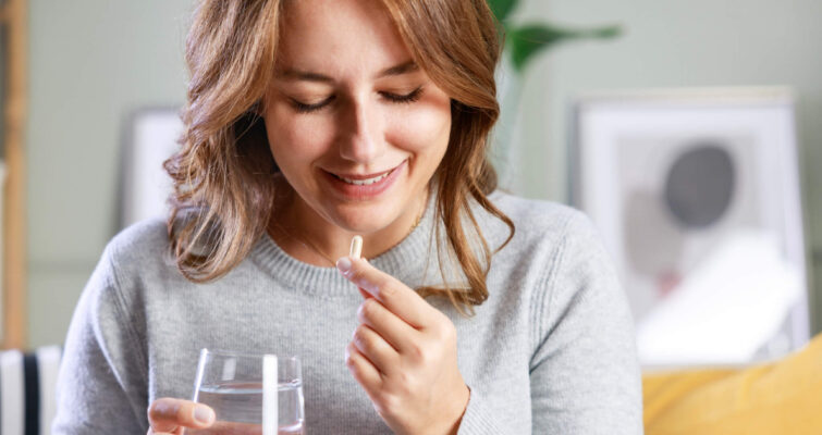 A woman smiles while holding a glass of water, conveying a sense of joy and refreshment.