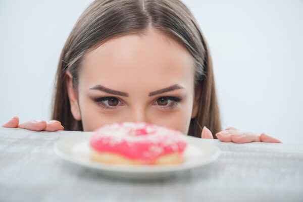 A woman looks over a plate, her expression curious as she observes a pink donut on it.
