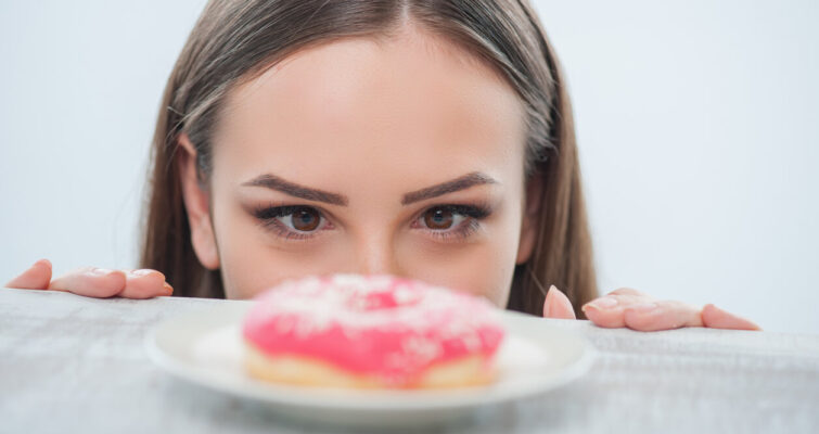 A woman looks over a plate, her expression curious as she observes a pink donut on it.