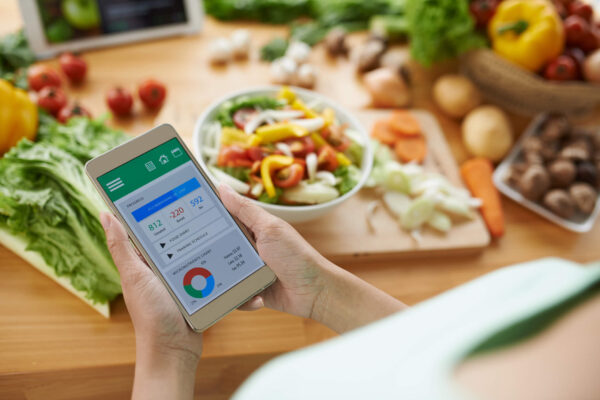 Woman checking her smartphone to track her diet and health progress while sitting at a table.