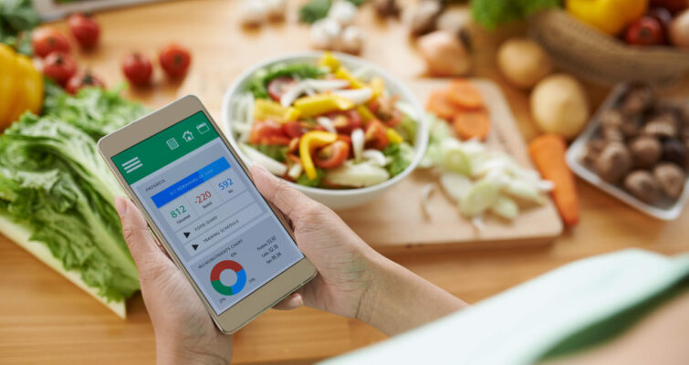 Woman checking her smartphone to track her diet and health progress while sitting at a table.