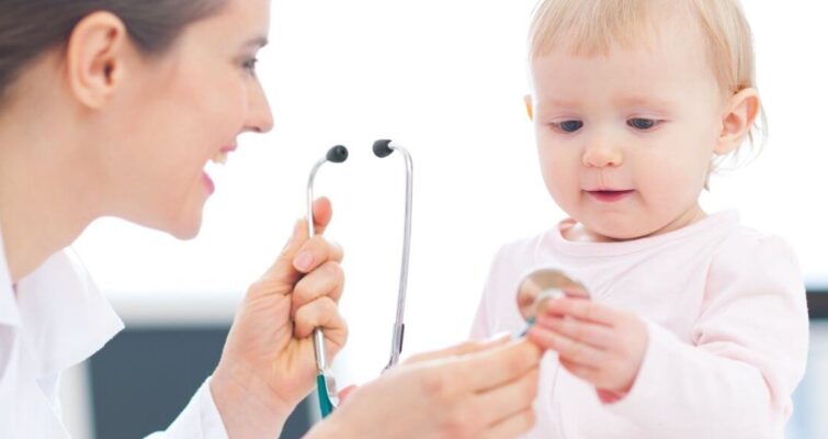 A woman holds a baby while examining a stethoscope, illustrating the role of integrative pediatricians in healthcare.