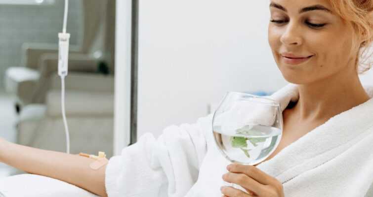 A woman in a bathrobe holds a glass of water, representing IV Vitamin Therapy options in Atlanta.