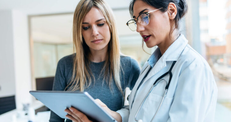 Two female doctors examining a tablet, discussing health concerns related to cancer in millennials.