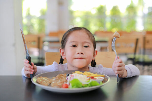 A little girl holding a fork and knife, symbolizing the importance of healthy eating for gut health awareness.