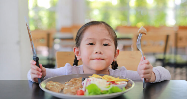 A little girl holding a fork and knife, symbolizing the importance of healthy eating for gut health awareness.