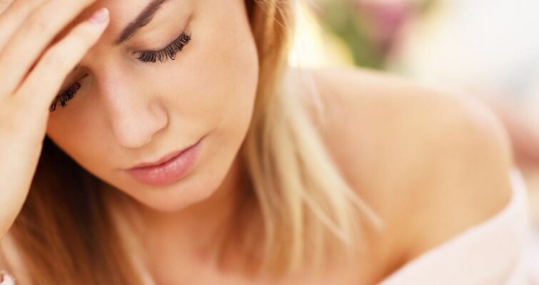 A woman holds her head in pain, illustrating the discomfort associated with low progesterone side effects.