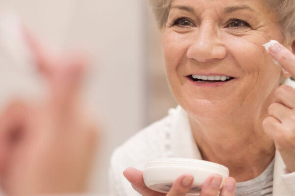 An older woman examines her reflection in a mirror, highlighting the importance of skincare for mature skin.