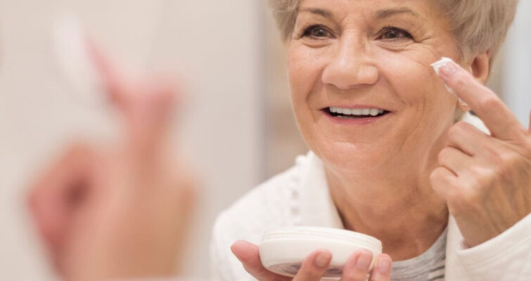 An older woman examines her reflection in a mirror, highlighting the importance of skincare for mature skin.