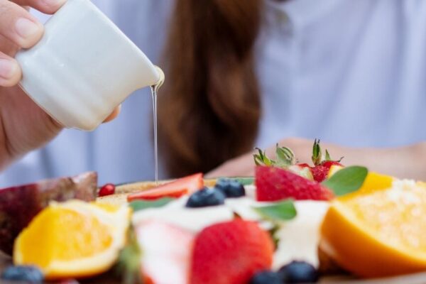 A woman holds a spoon over a plate of colorful fruit, highlighting healthy antibacterial food choices for better eating.