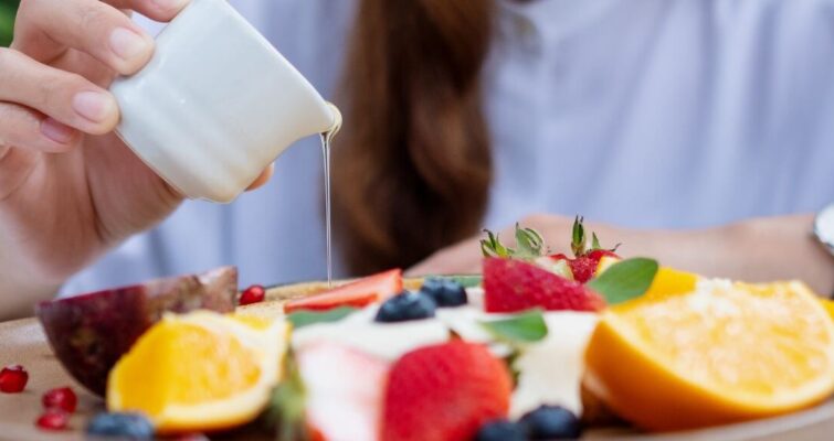 A woman holds a spoon over a plate of colorful fruit, highlighting healthy antibacterial food choices for better eating.