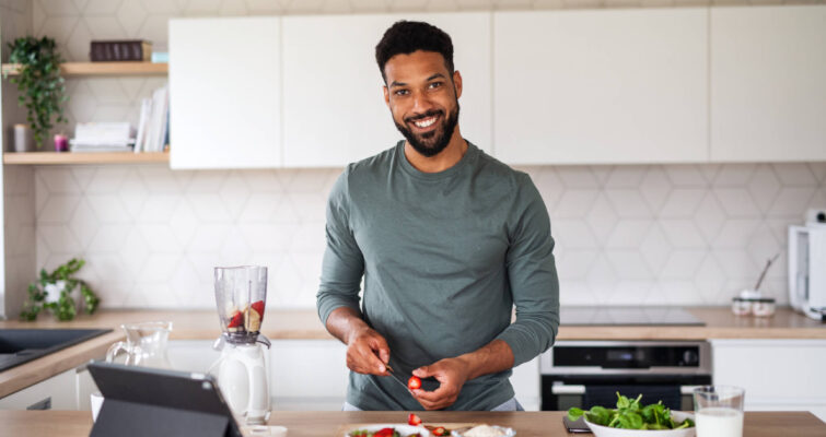 Smiling man in a kitchen, surrounded by healthy food and a tablet, emphasizing cardiometabolic health awareness.