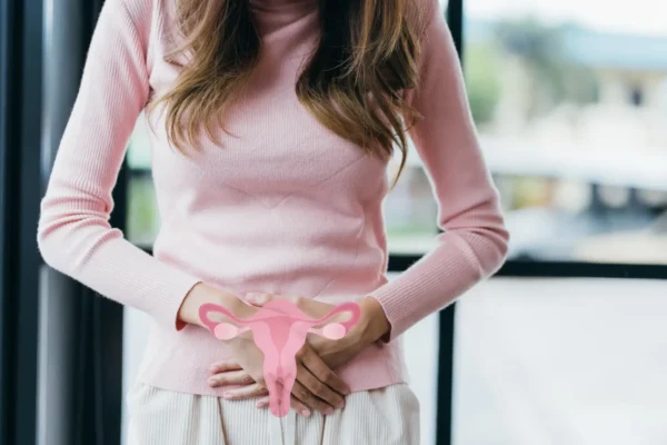 A woman holds her stomach while grasping a pink object, symbolizing issues related to PCOS and endometriosis