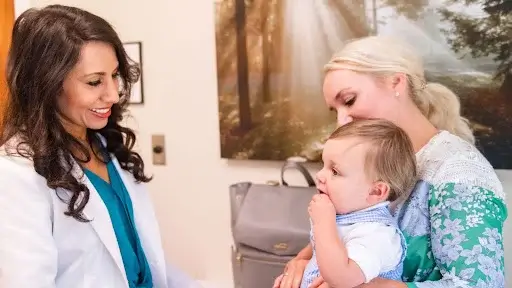 A woman holds a baby while discussing pediatric care with a doctor, emphasizing a holistic approach to health.