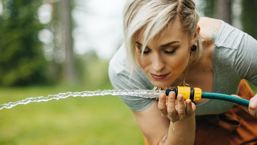 A woman waters her garden with a hose, nurturing her plants under bright sunlight.