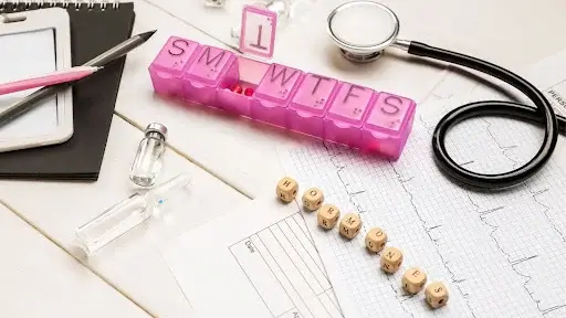 A stethoscope, pen, pill box, and calculator arranged on a surface, symbolizing health management and integrative medicine.