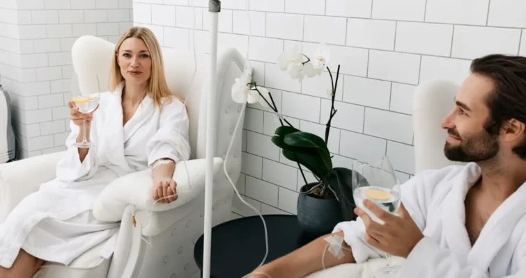 A man and woman in white robes relax in a serene spa room, highlighting the calming atmosphere of IV Vitamin C therapy.