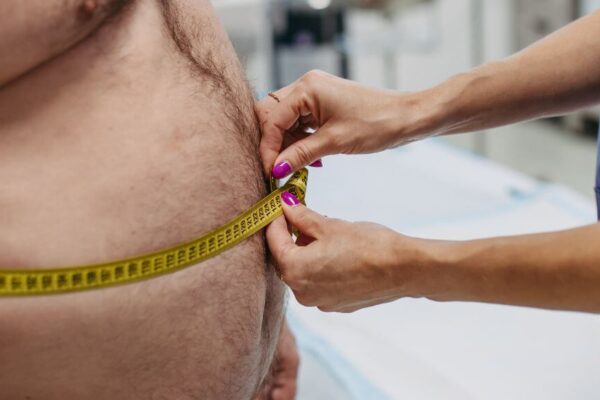 A man measuring his waist with a tape measure, illustrating the concept of sarcopenic obesity and its treatment.
