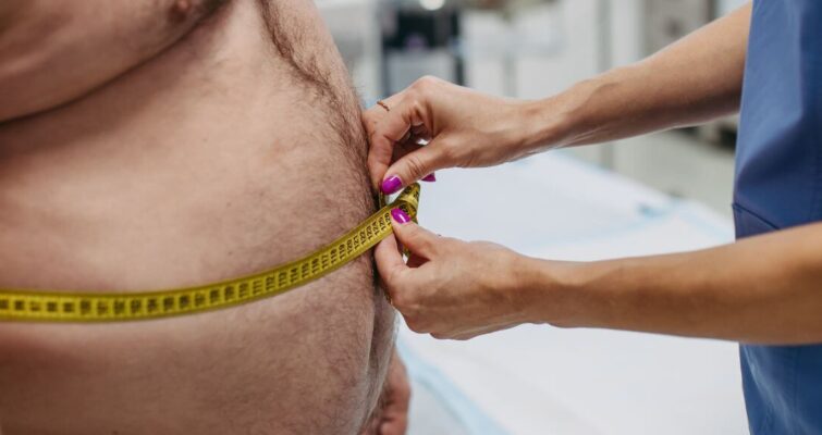 A man measuring his waist with a tape measure, illustrating the concept of sarcopenic obesity and its treatment.
