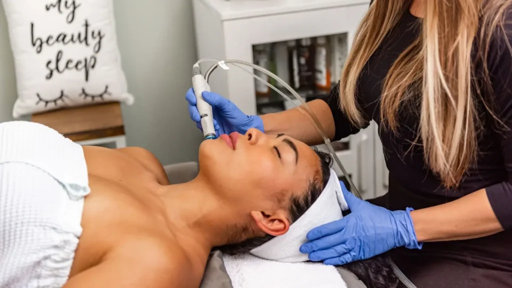 A person is receiving a facial treatment while lying on a massage table, with a technician using a device on their face.