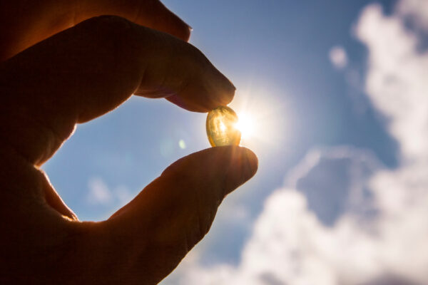 A person holds a fish oil capsule, highlighting its role in vitamin D intake for skin cancer prevention.
