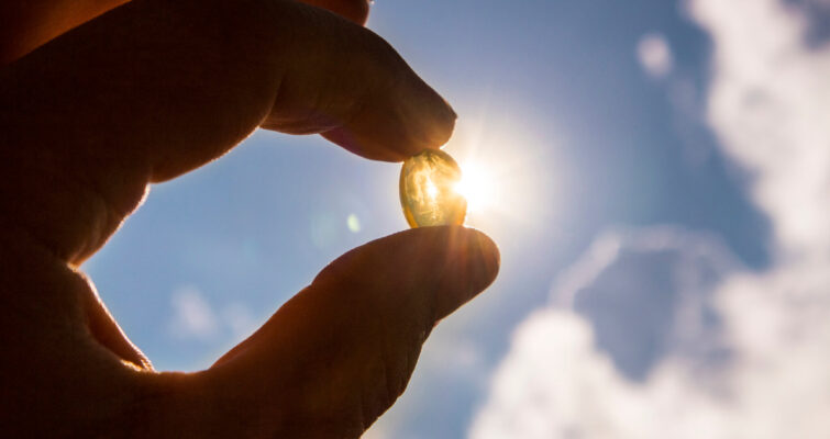 A person holds a fish oil capsule, highlighting its role in vitamin D intake for skin cancer prevention.