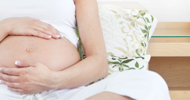 A pregnant woman sitting on a couch, reflecting on the benefits of acupuncture during pregnancy for prenatal health.
