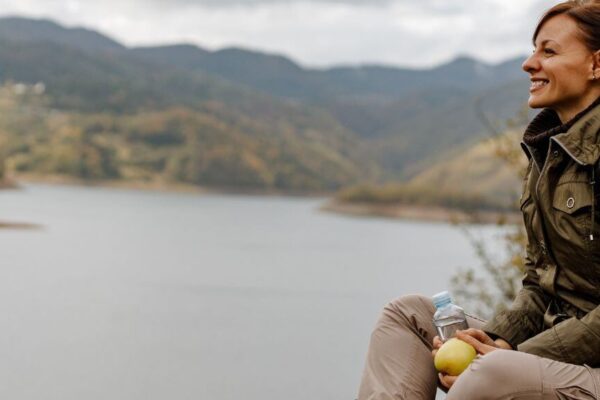 A woman sits on a hill, gazing at a serene lake, reflecting on the benefits of holistic medicine for health.