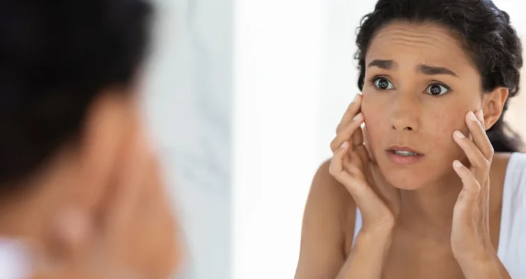 A woman examines her face in the mirror, reflecting concerns about dry skin and omega-3 deficiency signs.