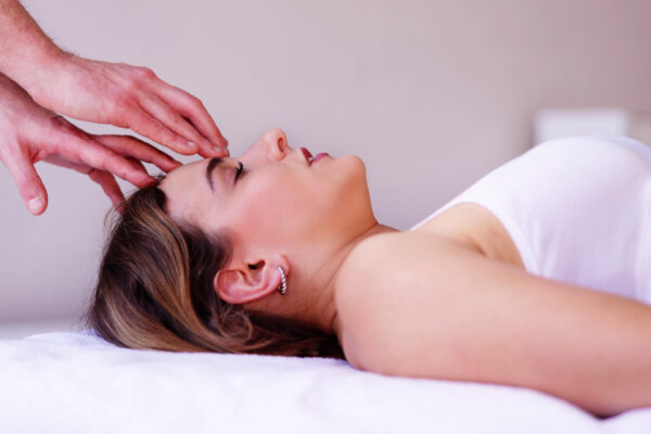 A woman lies on her back with hands on her forehead, embodying tranquility in a healing energy session.