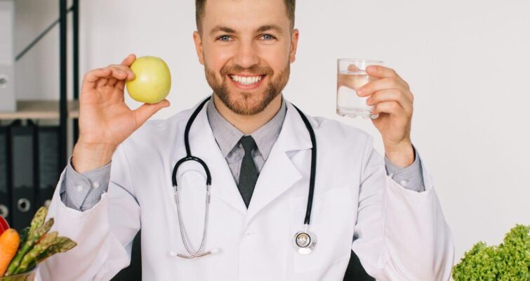 A man in a white coat holds an apple and a glass of water, symbolizing holistic and functional medicine approaches.