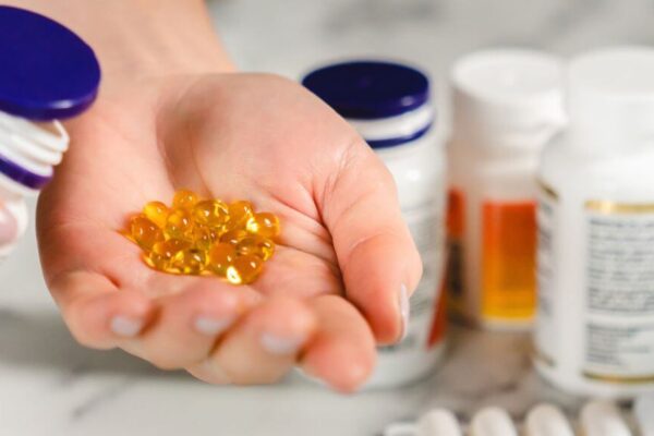 A person holding a bottle of hormone balancing supplements and several pills in their hand