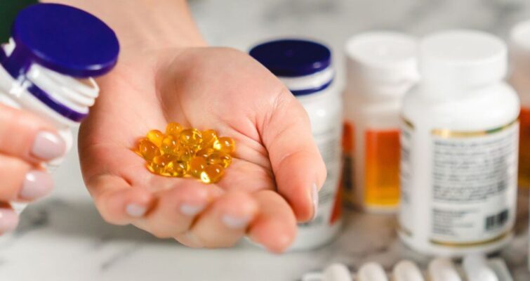 A person holding a bottle of hormone balancing supplements and several pills in their hand