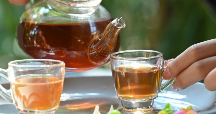 A person pours tea into two glasses, highlighting the theme of hormone balancing with the best teas.