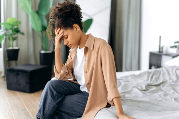 A woman sitting on a bed, holding her head in her hands, reflecting the struggle of morning migraine triggers.