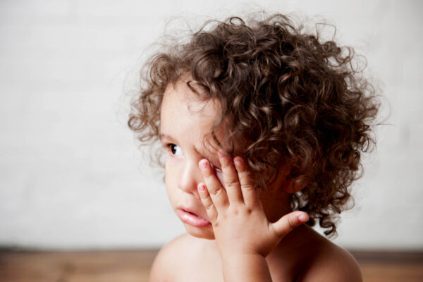A young child with curly hair obscuring his eyes, featured in a discussion about natural pink eye remedies.