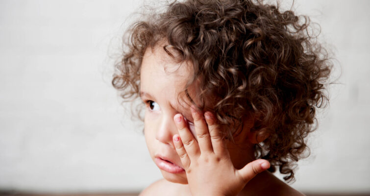 A young child with curly hair obscuring his eyes, featured in a discussion about natural pink eye remedies.