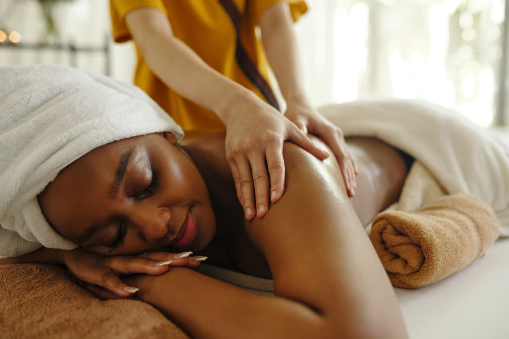 A person receives a massage while resting on a treatment table, with a towel wrapped around their hair.