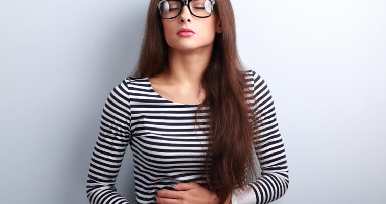 A woman clutches her stomach in discomfort, related to the theme of leaky gut with Landria Voigt.