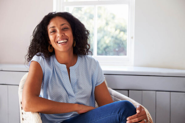 A smiling woman sitting in a chair, promoting hormone balance.