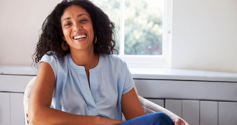 A smiling woman sitting in a chair, promoting hormone balance.