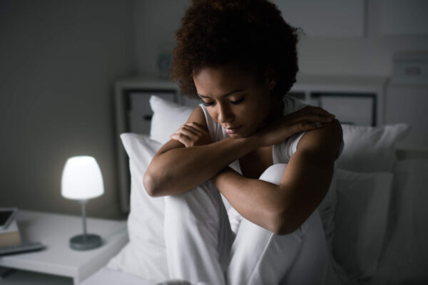 A woman sitting on a bed with her hands on her knees, reflecting on symptoms of low progesterone.