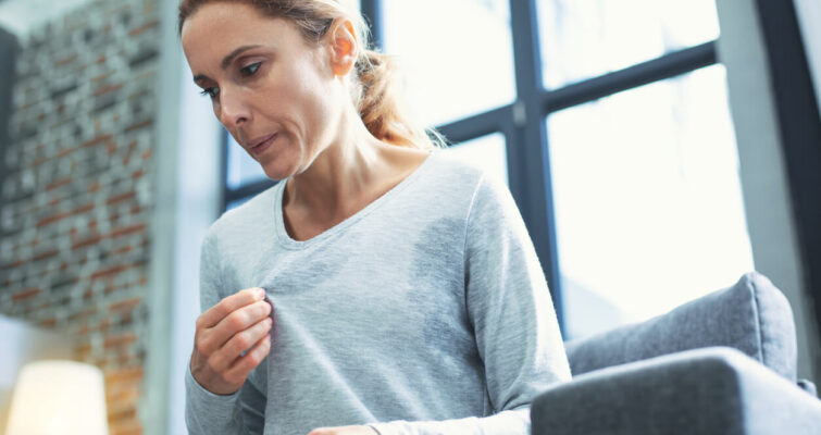 A woman sitting on a couch, hands on her stomach, reflecting on topics from The Integrative Medicine Guide to Perimenopause.