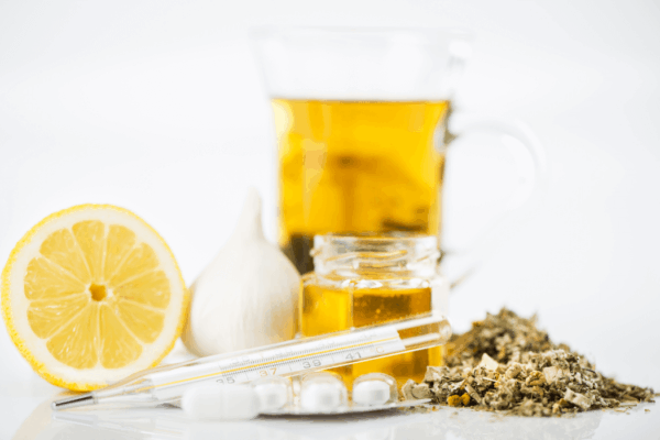 A glass of tea with lemon and pills, representing immune supplements for cold and flu season preparation.