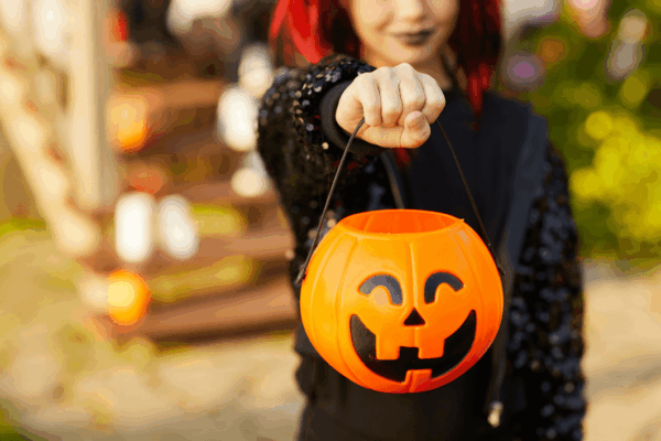 A woman holds a pumpkin-shaped Halloween candy bucket, promoting a healthy approach to Halloween treats.