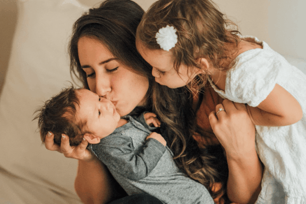 Mom and baby share a loving kiss on a bed, highlighting their bond and affection in a cozy setting.
