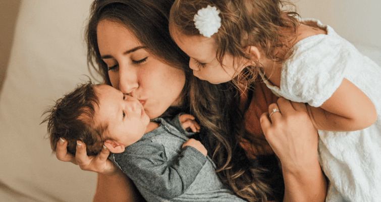 Mom and baby share a loving kiss on a bed, highlighting their bond and affection in a cozy setting.