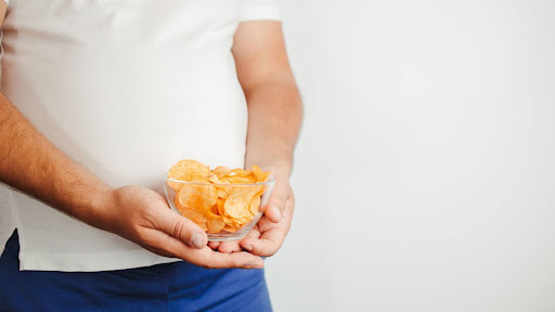 A man holds a glass filled with chips, illustrating dietary choices affecting testosterone levels in men.