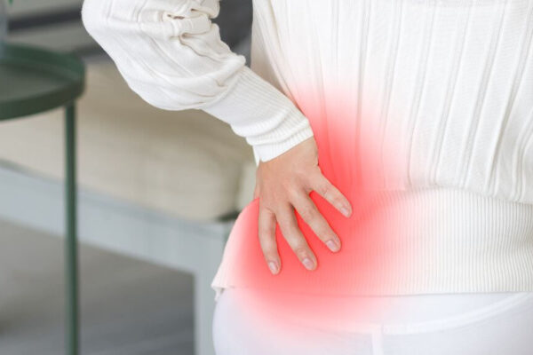A woman sitting on a couch, visibly in discomfort, holding her lower back, illustrating back pain related to osteoporosis.