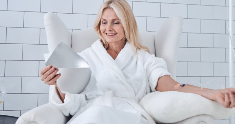 A woman in a bathrobe sits in a chair, reflecting on the pros and cons of IV vitamin therapy.
